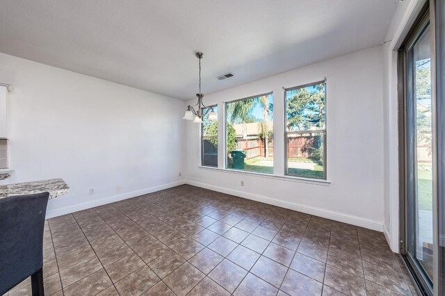 unfurnished dining area featuring dark tile patterned flooring, a notable chandelier, and a wealth of natural light