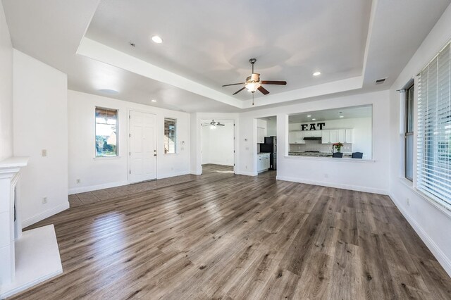 unfurnished living room featuring a tray ceiling, hardwood / wood-style flooring, and ceiling fan