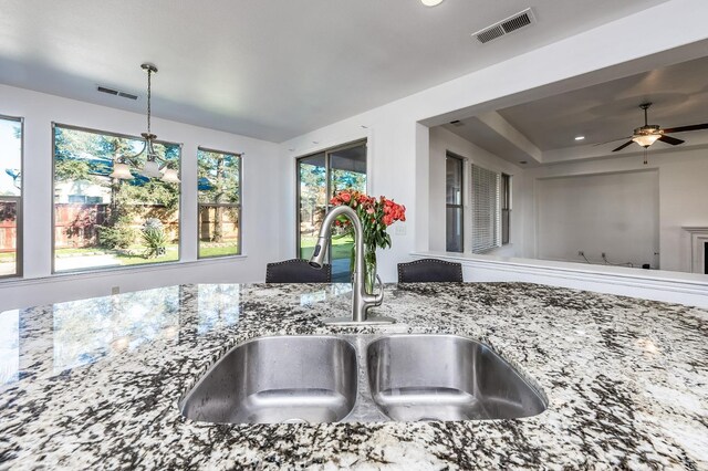 interior details featuring stone counters, sink, ceiling fan, and hanging light fixtures