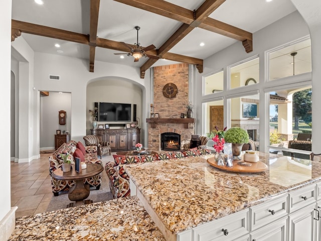 living room featuring coffered ceiling, a stone fireplace, ceiling fan, a towering ceiling, and beamed ceiling