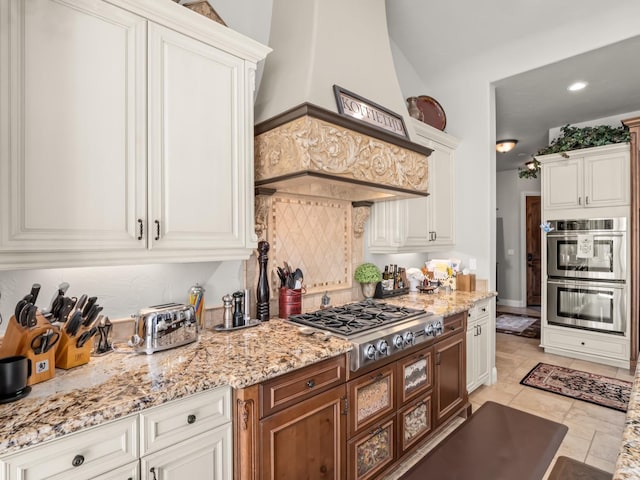 kitchen featuring white cabinets, appliances with stainless steel finishes, light stone countertops, and custom range hood