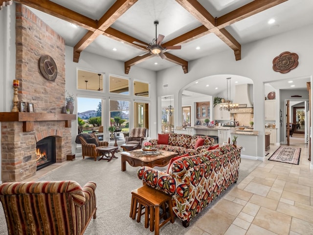 living room featuring a towering ceiling, a fireplace, coffered ceiling, ceiling fan with notable chandelier, and beamed ceiling