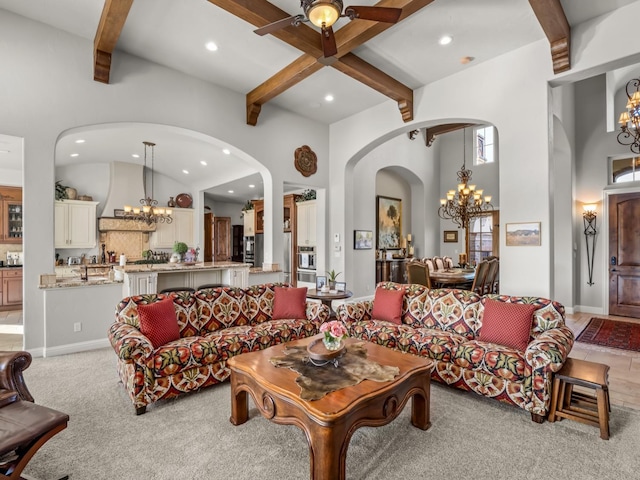 living room featuring a towering ceiling, beamed ceiling, light colored carpet, and ceiling fan with notable chandelier