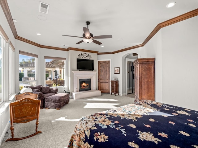 bedroom featuring ceiling fan, light colored carpet, crown molding, and a tiled fireplace