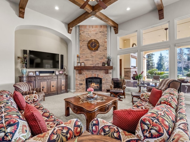 carpeted living room with beam ceiling, a stone fireplace, and ceiling fan