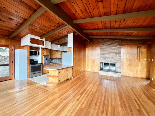 kitchen featuring kitchen peninsula, appliances with stainless steel finishes, decorative backsplash, a fireplace, and lofted ceiling with beams