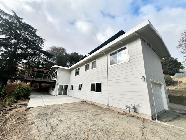 view of property exterior featuring a garage, a wooden deck, and a patio