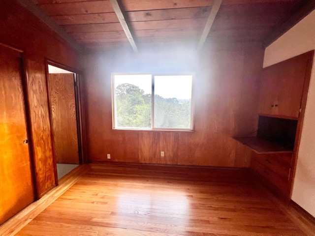 unfurnished bedroom with light hardwood / wood-style floors, beam ceiling, wood walls, and wood ceiling