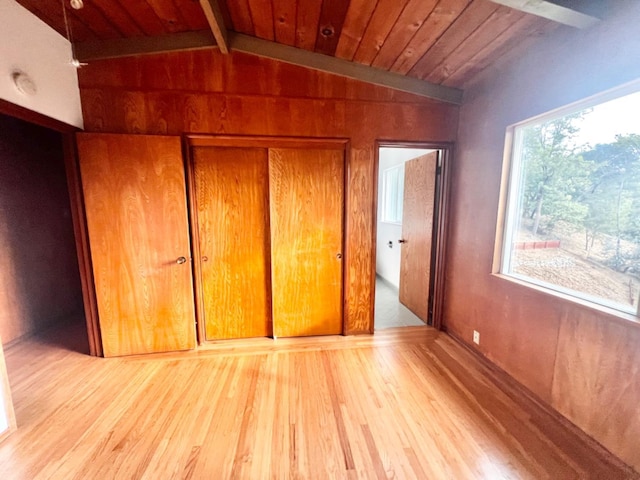 unfurnished bedroom featuring wooden ceiling, vaulted ceiling with beams, a closet, and light hardwood / wood-style floors