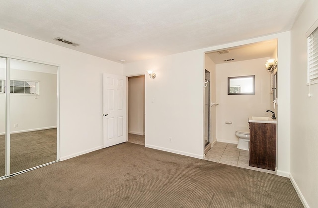 unfurnished bedroom with a closet, ensuite bath, sink, a textured ceiling, and carpet