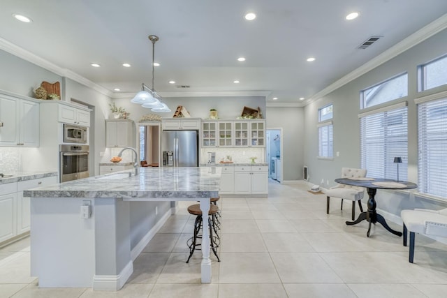 kitchen featuring a large island with sink, decorative backsplash, appliances with stainless steel finishes, decorative light fixtures, and white cabinetry