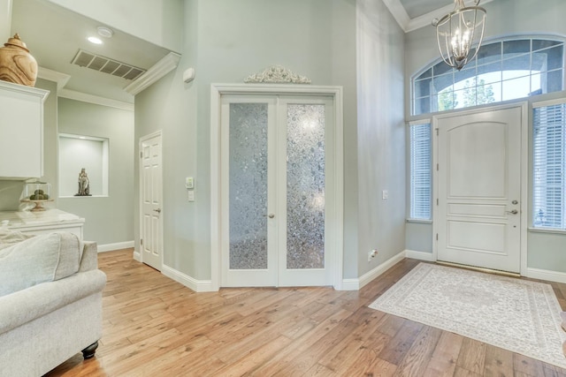 foyer entrance featuring a notable chandelier, ornamental molding, a towering ceiling, and light hardwood / wood-style flooring