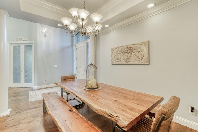 dining space featuring french doors, a notable chandelier, crown molding, a tray ceiling, and light wood-type flooring