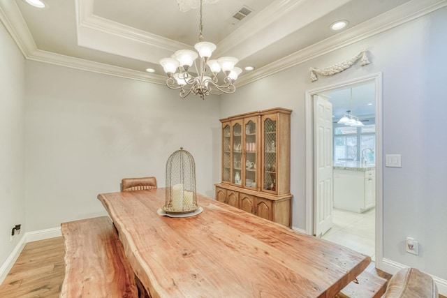 dining space with a notable chandelier, light hardwood / wood-style floors, a raised ceiling, and crown molding