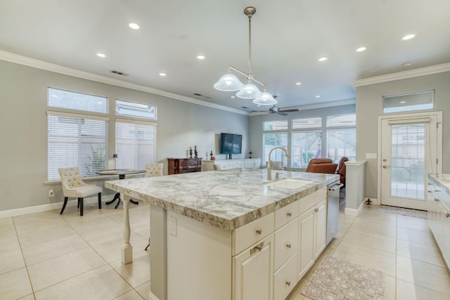 kitchen with ceiling fan, sink, hanging light fixtures, light stone counters, and an island with sink