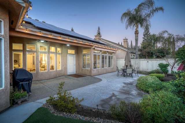 back house at dusk featuring solar panels and a patio