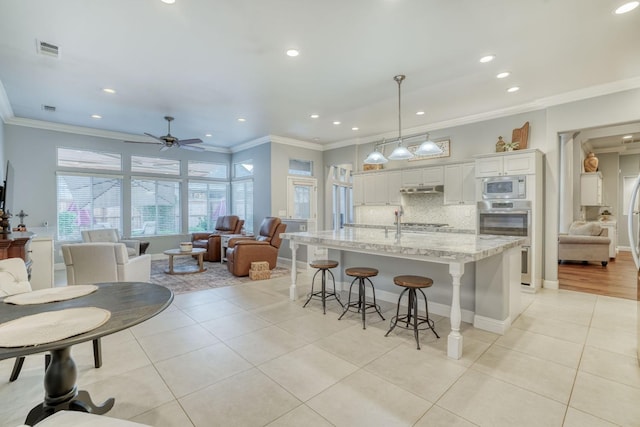 kitchen with appliances with stainless steel finishes, ceiling fan, a large island with sink, decorative light fixtures, and white cabinetry