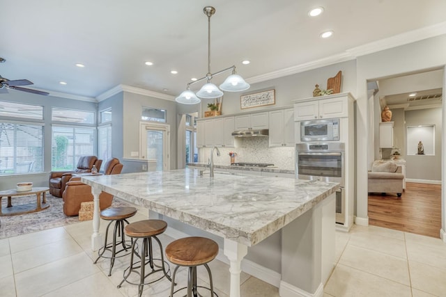 kitchen featuring appliances with stainless steel finishes, light tile patterned floors, a large island with sink, decorative light fixtures, and white cabinets