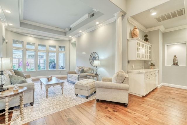 living room featuring light hardwood / wood-style floors, crown molding, a tray ceiling, and decorative columns