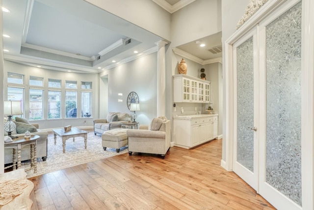 living area featuring light wood-type flooring, a tray ceiling, ornate columns, and ornamental molding