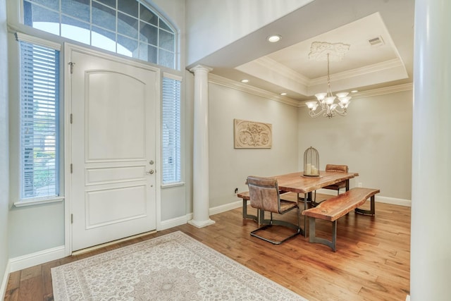 foyer entrance featuring decorative columns, a raised ceiling, hardwood / wood-style floors, and a chandelier