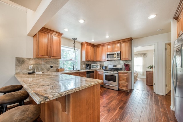 kitchen with kitchen peninsula, hanging light fixtures, stainless steel appliances, and a breakfast bar