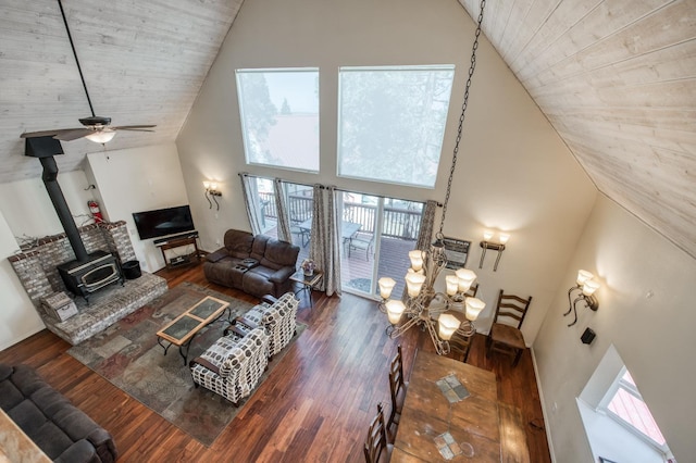 living room with a wood stove, high vaulted ceiling, dark wood-type flooring, and ceiling fan with notable chandelier