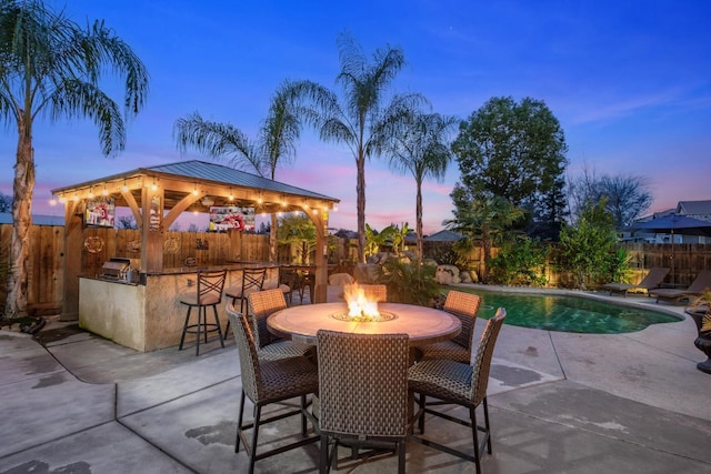 patio terrace at dusk with a gazebo, a fenced in pool, an outdoor bar, and a grill