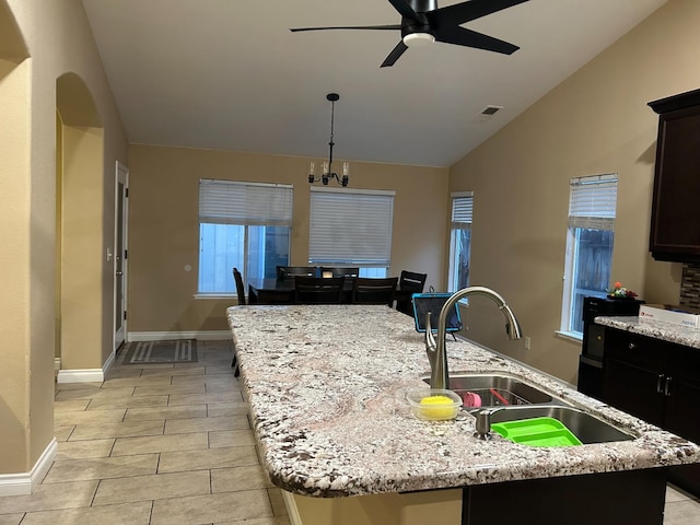 kitchen featuring a center island with sink, light stone countertops, sink, and vaulted ceiling