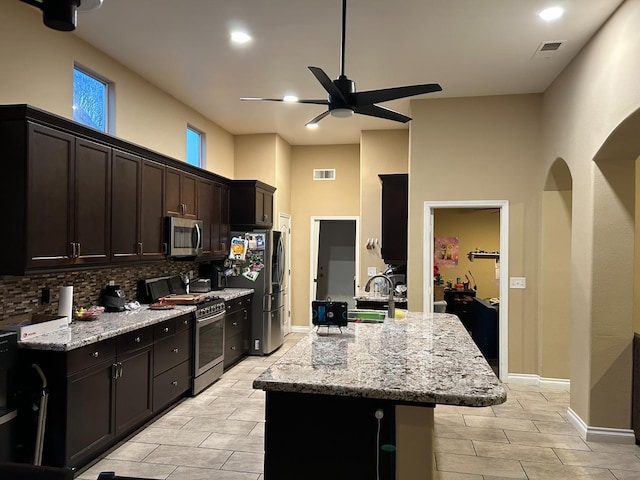 kitchen with light stone countertops, backsplash, stainless steel appliances, ceiling fan, and sink