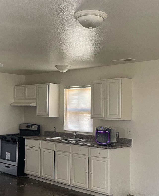 kitchen featuring stainless steel gas range, dark countertops, a sink, and white cabinetry