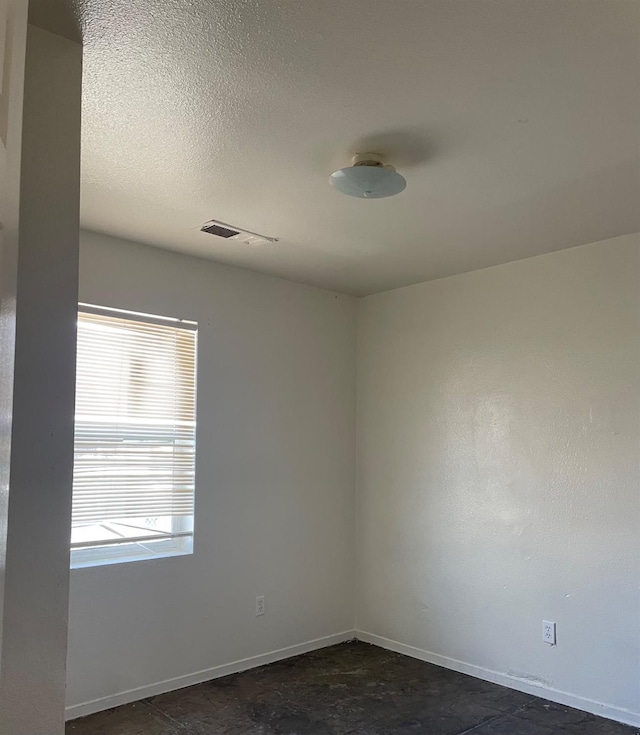 unfurnished room with visible vents, a textured ceiling, and baseboards