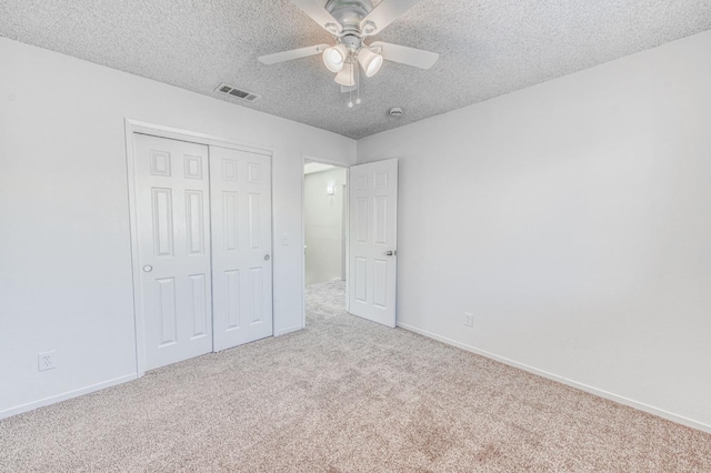 unfurnished bedroom featuring light carpet, a textured ceiling, a closet, and ceiling fan