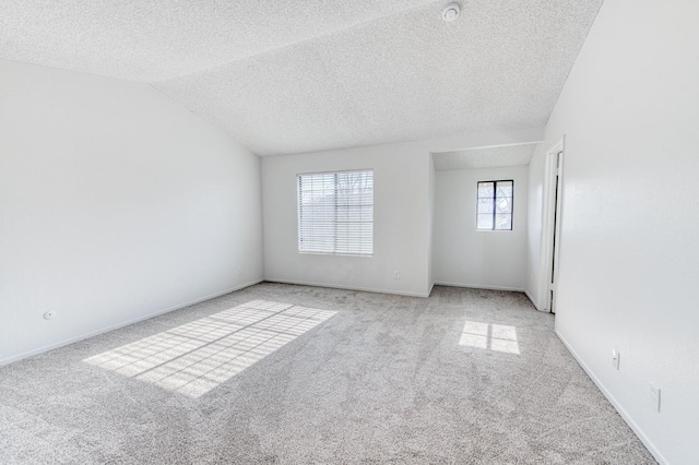 carpeted spare room featuring a textured ceiling, plenty of natural light, and vaulted ceiling