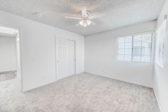 unfurnished bedroom featuring ceiling fan, light colored carpet, a textured ceiling, and a closet