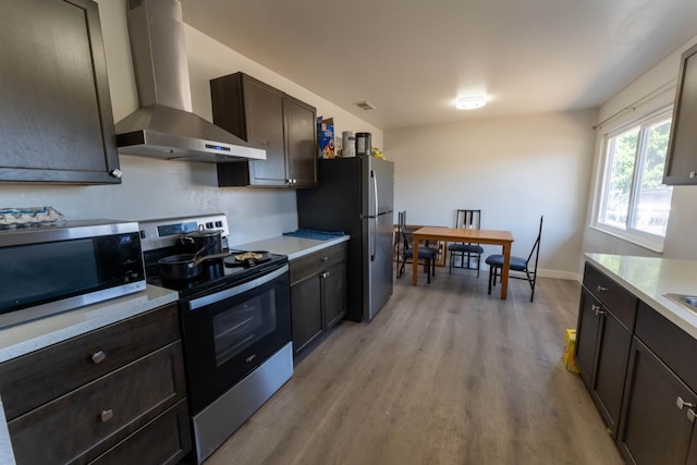 kitchen with dark brown cabinetry, light hardwood / wood-style flooring, stainless steel appliances, and wall chimney range hood