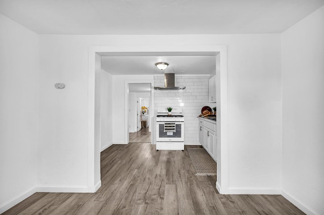 kitchen featuring gas range gas stove, wall chimney exhaust hood, decorative backsplash, white cabinets, and hardwood / wood-style flooring