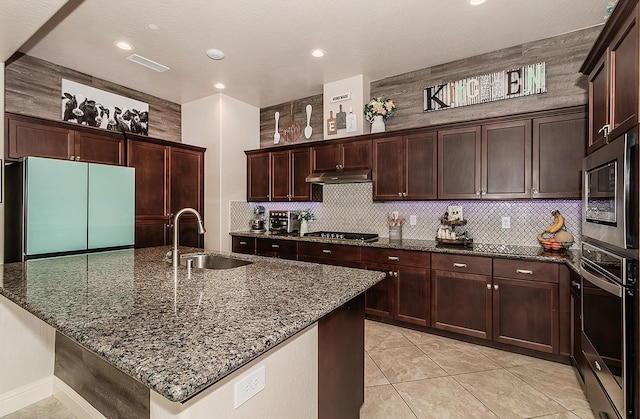 kitchen with dark stone counters, sink, light tile patterned floors, appliances with stainless steel finishes, and dark brown cabinetry