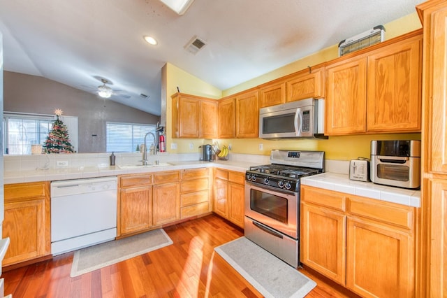 kitchen with sink, stainless steel appliances, light hardwood / wood-style flooring, tile countertops, and vaulted ceiling