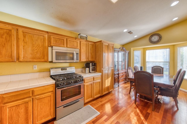 kitchen with appliances with stainless steel finishes, light hardwood / wood-style flooring, vaulted ceiling, and tile counters