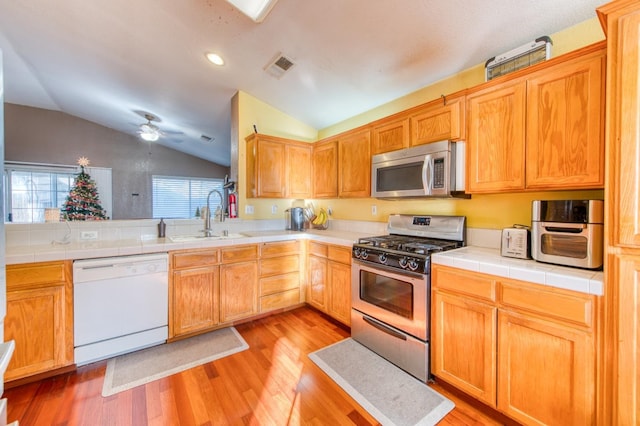 kitchen with tile counters, light hardwood / wood-style floors, appliances with stainless steel finishes, and vaulted ceiling