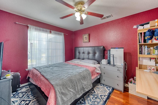 bedroom featuring radiator, ceiling fan, hardwood / wood-style floors, and a textured ceiling