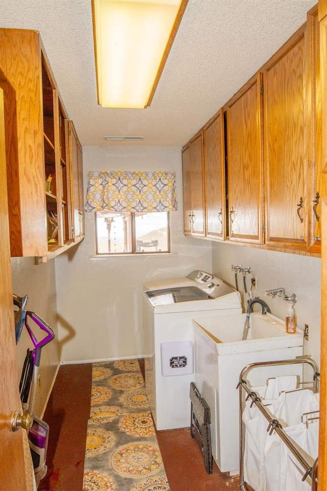 washroom with washing machine and dryer, a textured ceiling, and cabinets