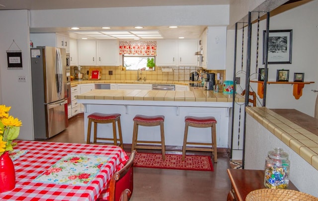 kitchen featuring a breakfast bar, appliances with stainless steel finishes, tile countertops, and white cabinetry