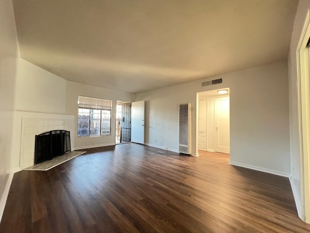 unfurnished living room featuring a tile fireplace and dark hardwood / wood-style floors