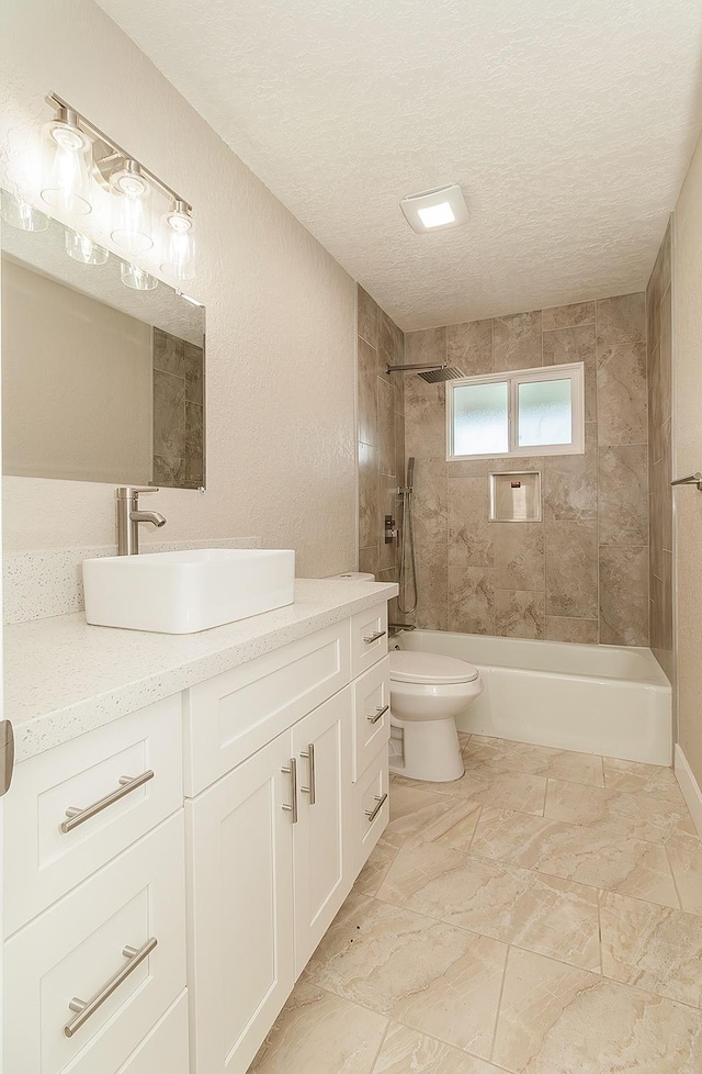 full bathroom with tiled shower / bath, vanity, toilet, and a textured ceiling