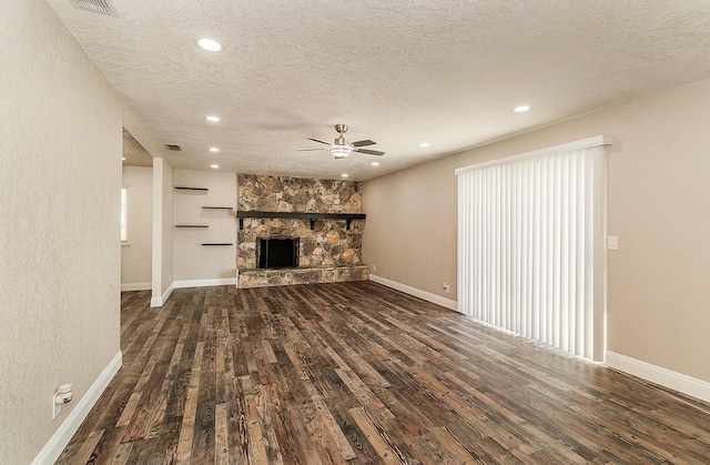 unfurnished living room with a stone fireplace, a textured ceiling, and dark hardwood / wood-style flooring