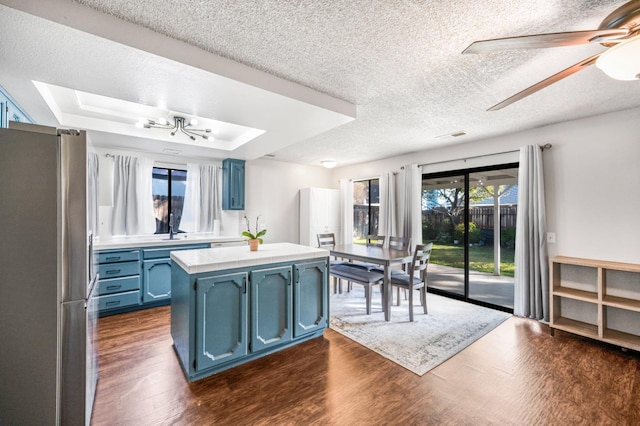 kitchen featuring ceiling fan, a raised ceiling, blue cabinets, and stainless steel refrigerator