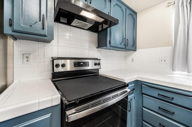 kitchen featuring backsplash, tile countertops, blue cabinets, and stainless steel range with electric stovetop