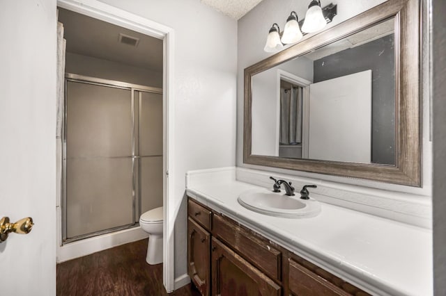 bathroom featuring wood-type flooring, a textured ceiling, an enclosed shower, toilet, and vanity